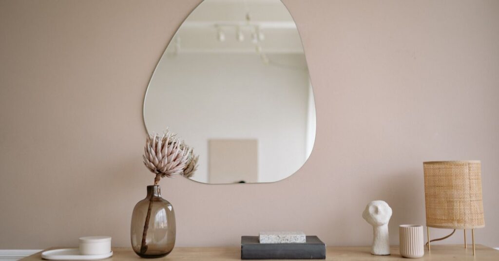 Minimal decor setup with mirror, vase, lamp, and books on a wooden table.