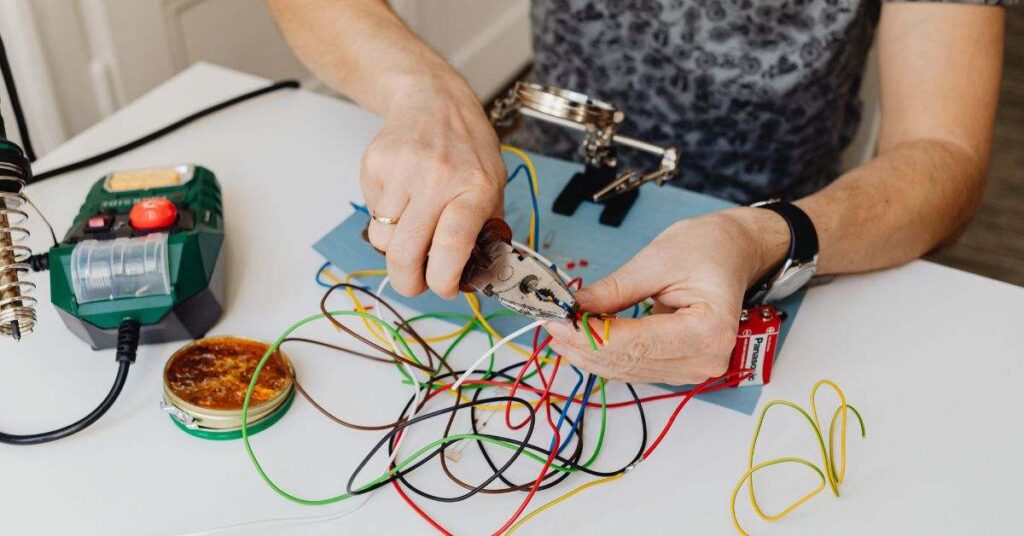 Hands using pliers to connect colorful wires on desk