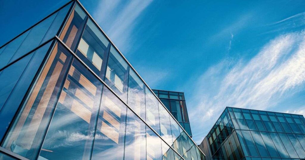 Modern glass office building with reflective windows against a blue sky.