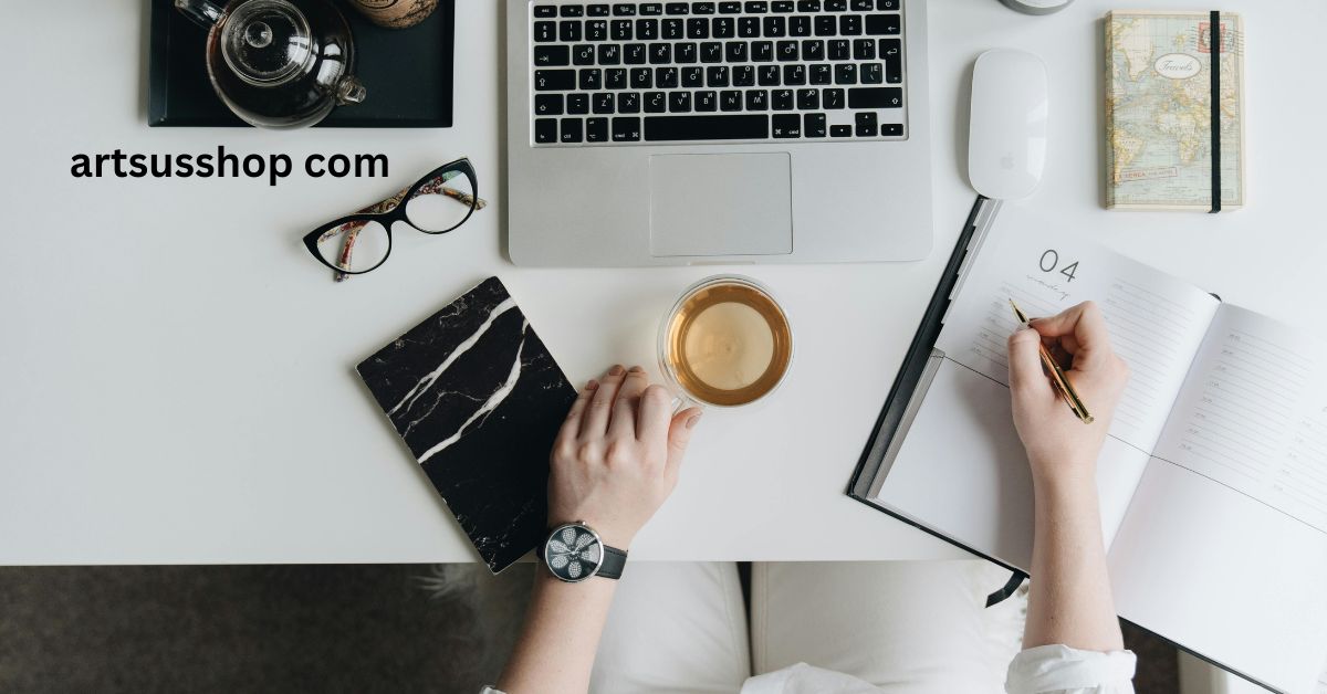 Minimal desk workspace with laptop, coffee, notebook, glasses, and hand writing notes.