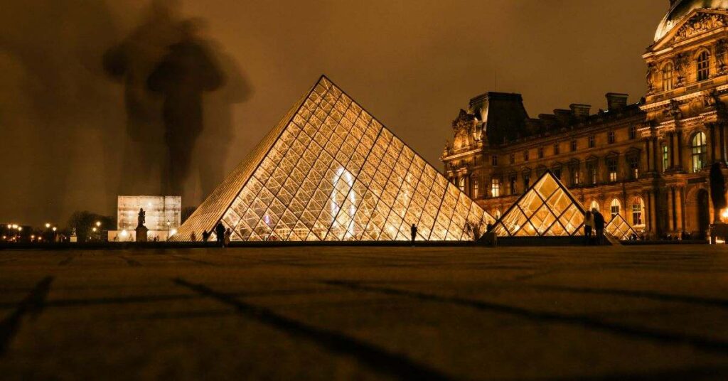 Louvre Pyramid at night glowing with golden lights in Paris courtyard