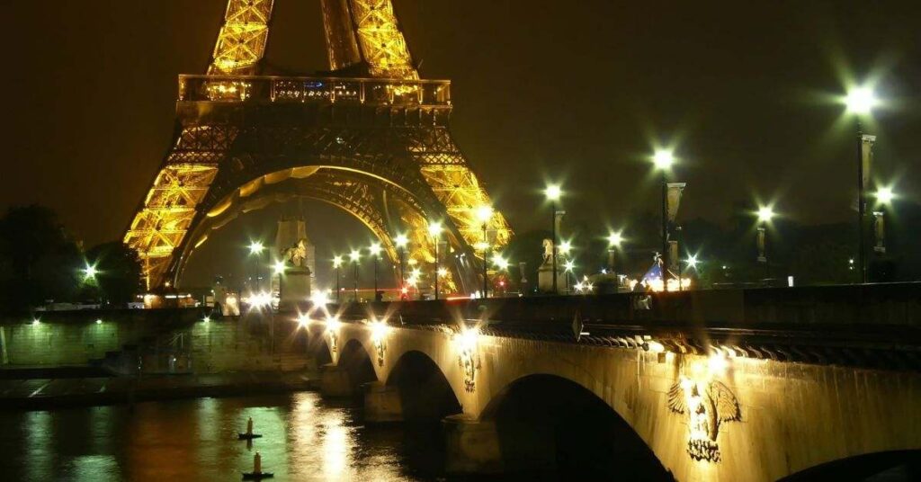 Eiffel Tower at night with bridge lights and river reflections in Paris
