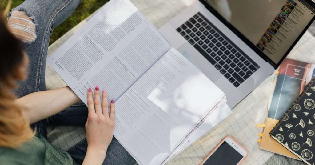 Student studying with open book, laptop, and notes, showing modern learning and digital education setup